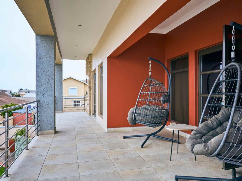 A spacious covered balcony featuring tiled flooring, modern stainless steel balustrades, and direct access to the interior through sliding glass doors.
