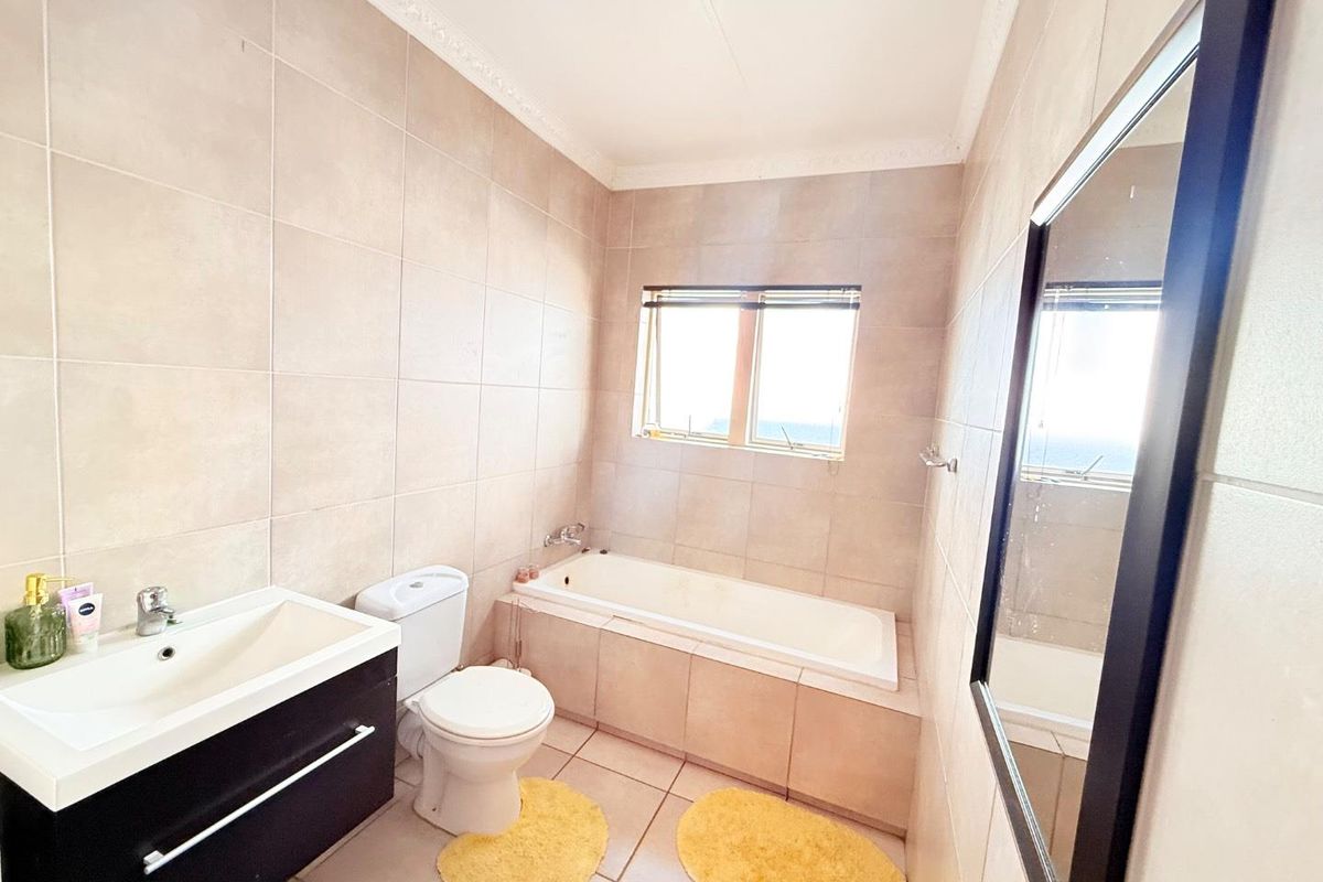 A well-maintained bathroom featuring neutral wall and floor tiling, a built-in bathtub, a modern vanity unit, and a toilet.