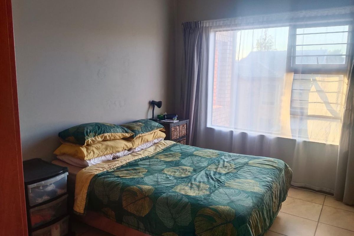 A functional bedroom featuring tiled flooring and a large window fitted with security bars, offering natural light.