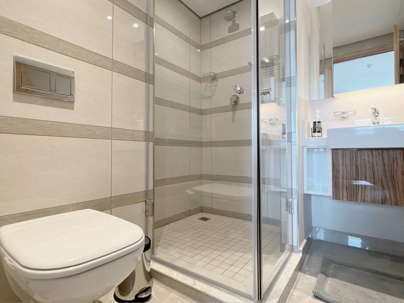 Modern bathroom featuring a glass-enclosed shower, wall-mounted toilet, and a contemporary vanity basin with tiled wall finishes.