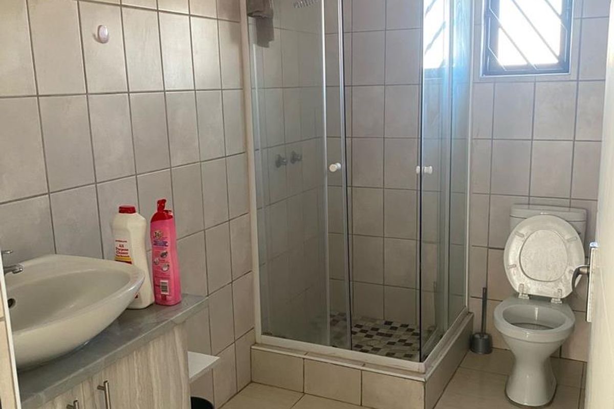 A functional bathroom featuring a corner shower enclosure, vanity cabinet with basin, and toilet, finished with neutral wall and floor tiles.
