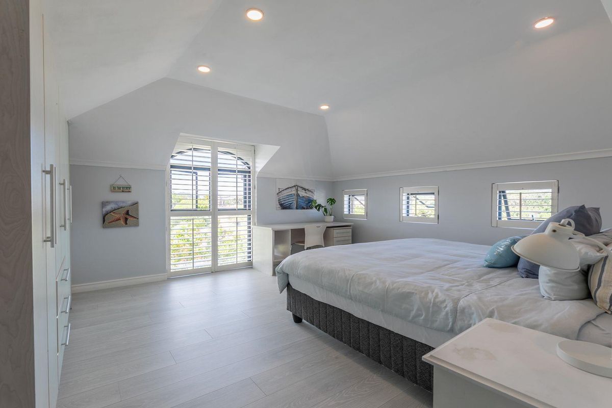 Spacious bedroom featuring vaulted ceilings, built-in cabinetry, light wood-look flooring, and plantation shutters on the windows.