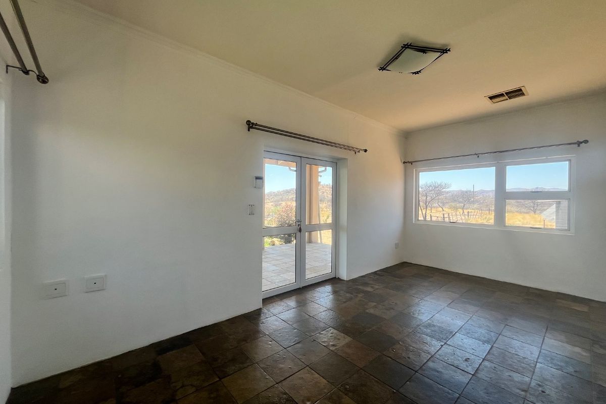 A bright, empty living room featuring dark tiled flooring, large windows with scenic views, and double glass doors leading to an outdoor patio area.