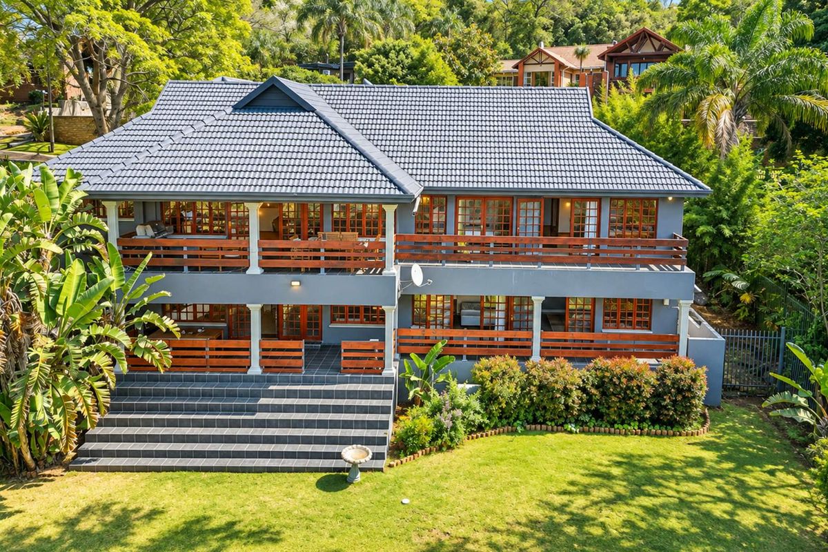 A well-maintained double-story residence featuring a tiled roof, expansive wooden balconies, and a spacious tiled staircase leading to a lush garden.