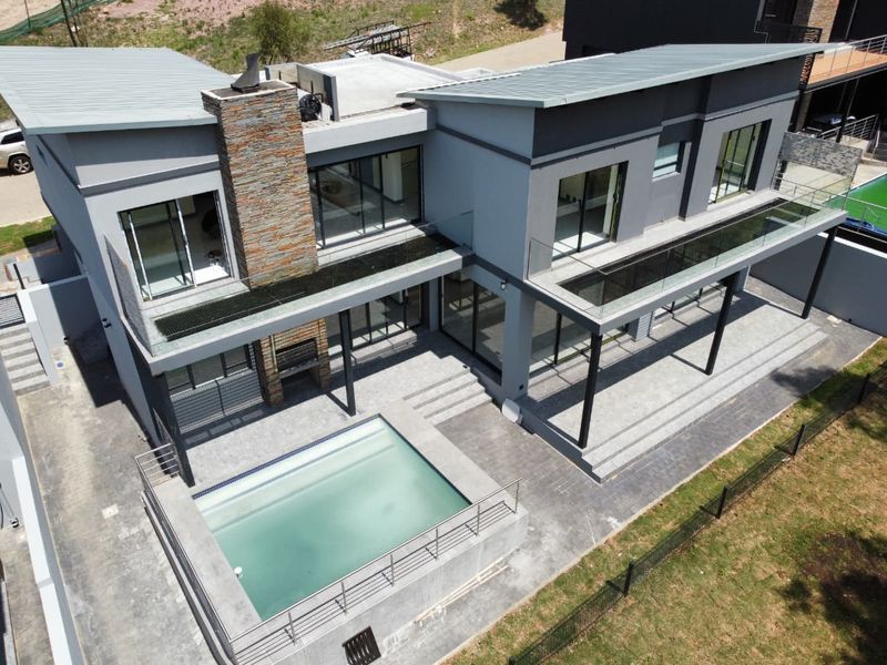 Aerial view of a modern double-story cluster home featuring a swimming pool, paved patio, built-in braai, and glass-railed balconies.