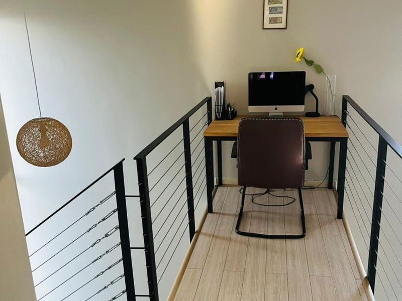 A compact landing area converted into a functional home office space, featuring modern wire railings and wood-look tile flooring.