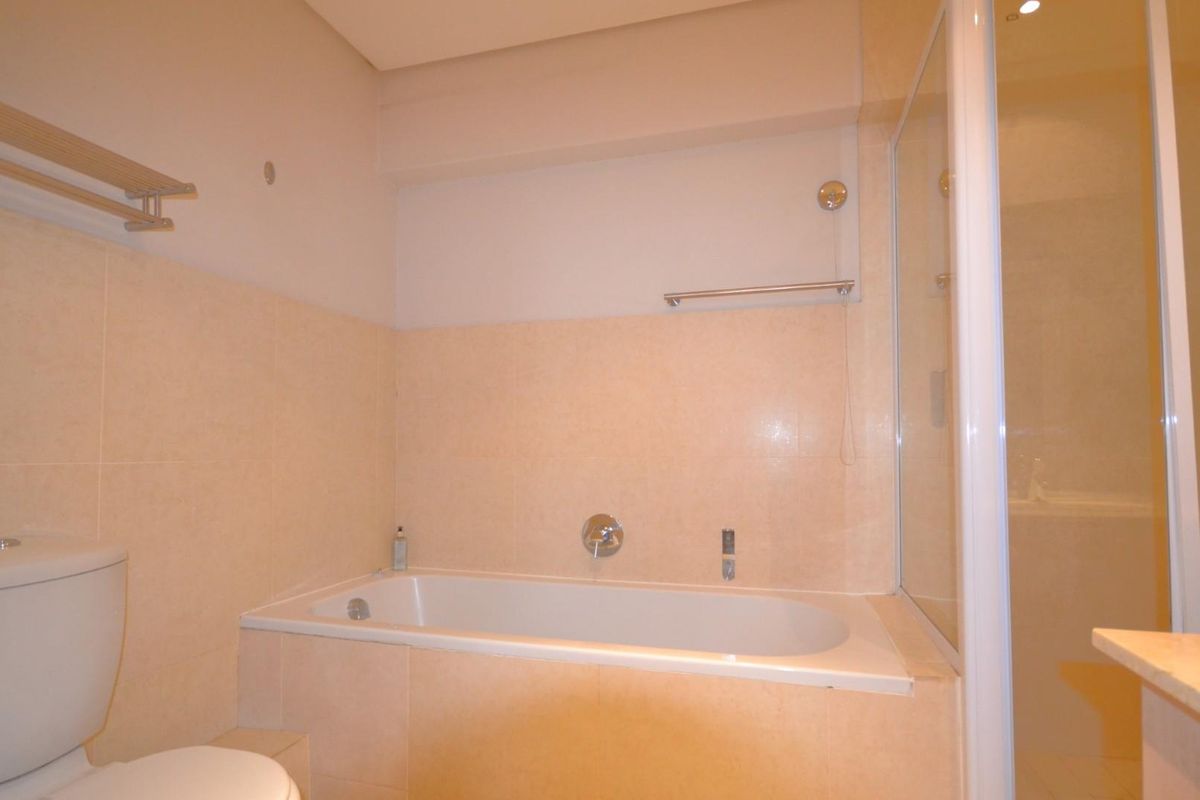 A functional bathroom featuring a built-in bathtub, separate shower enclosure, and neutral wall tiling.