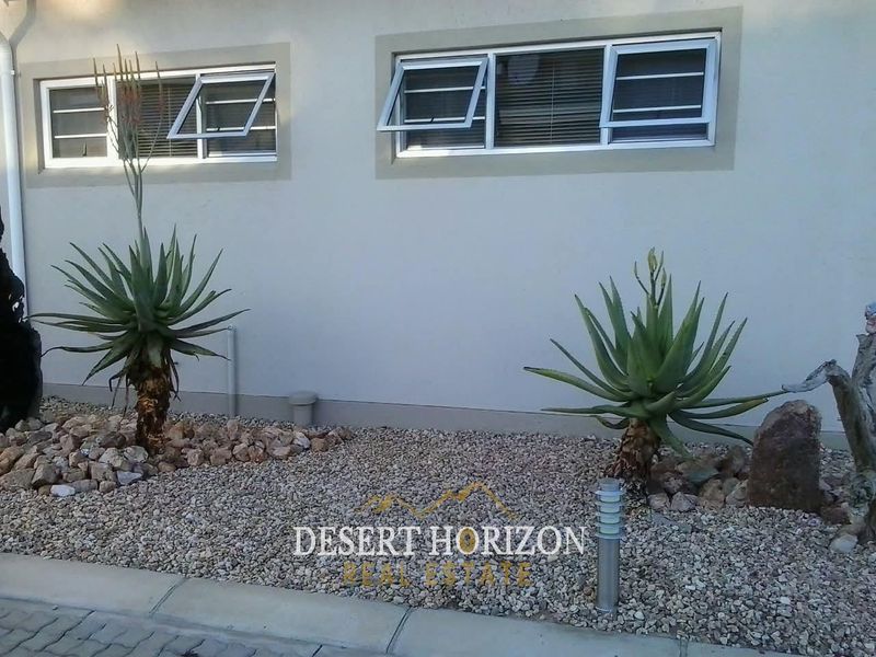 A view of the townhouse exterior featuring low-maintenance gravel landscaping, mature aloe plants, and modern aluminium top-hung windows.