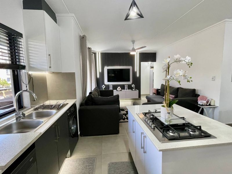 Modern open-plan living area featuring a sleek kitchen with a central island, gas hob, and contemporary finishes, seamlessly flowing into the lounge space.