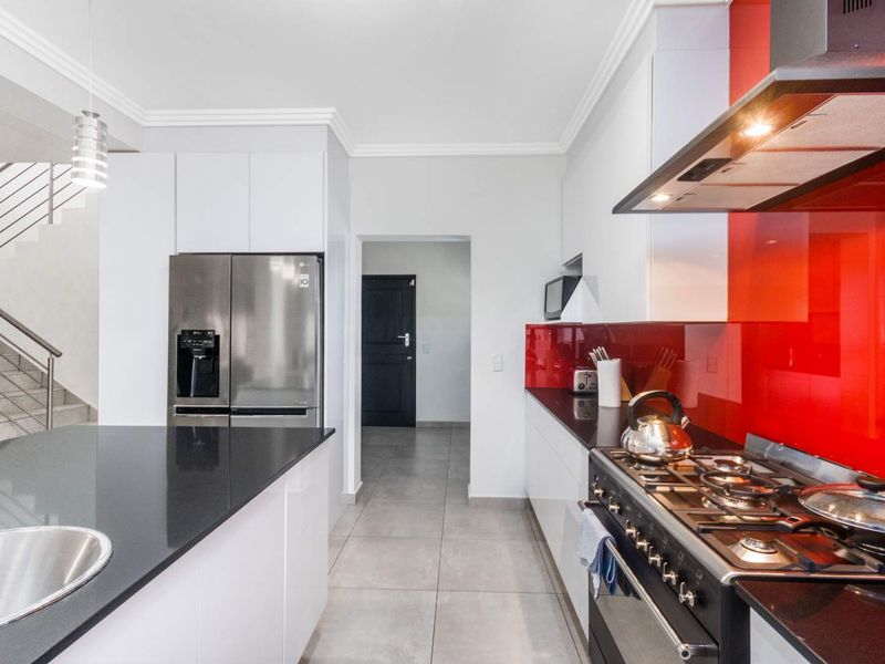 Modern kitchen featuring white cabinetry, black stone countertops, a striking red glass splashback, gas stove, and integrated stainless steel appliances.