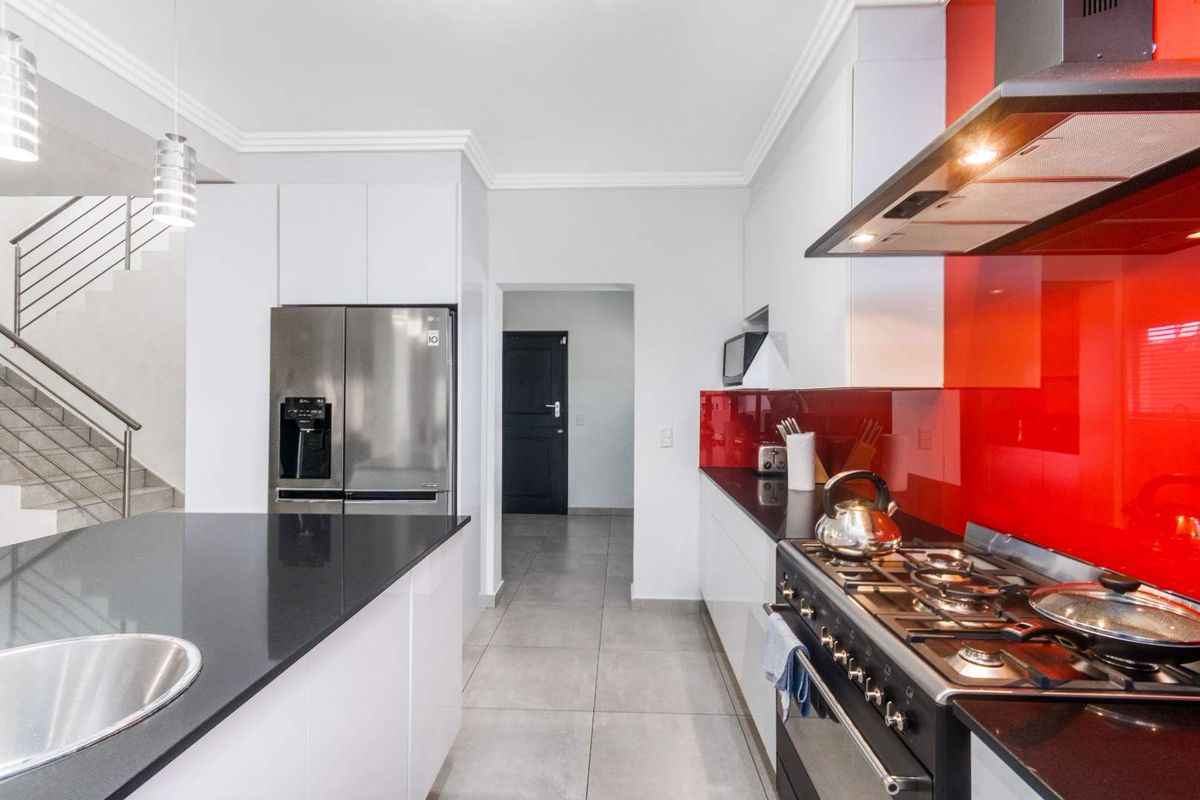 Modern kitchen featuring white cabinetry, black stone countertops, a striking red glass splashback, gas stove, and integrated stainless steel appliances.