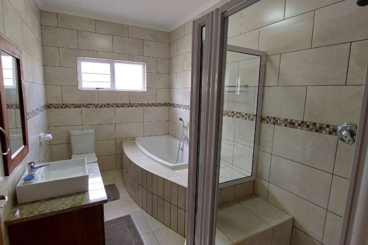 A well-maintained bathroom featuring a built-in bathtub, a separate glass-enclosed shower, a vanity with a basin, and tiled walls and flooring.
