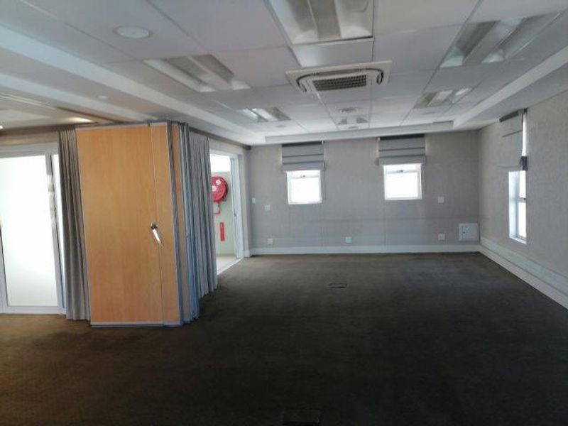 Spacious open-plan office area featuring a suspended ceiling, integrated cassette air conditioning, carpeted flooring, and a functional sliding partition wall for flexible space management.