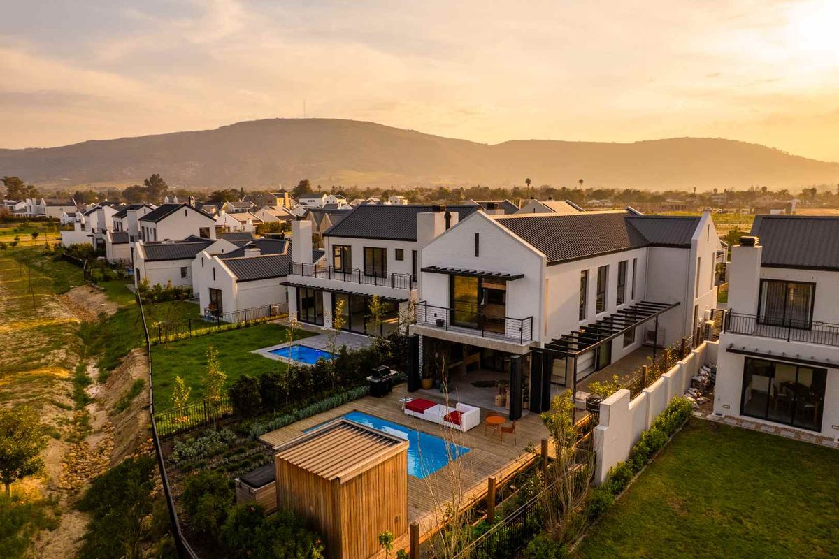 Aerial view of a modern residential property featuring a swimming pool, timber deck, and pergola, set within a well-maintained estate at sunset.