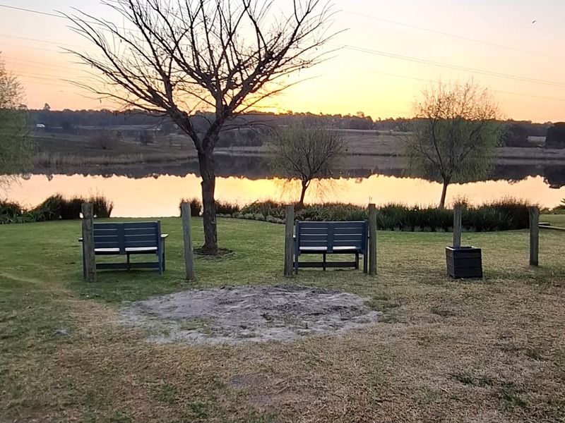 A scenic view of a tranquil lake at sunset, featuring a well-maintained grassy area with mature trees and natural landscaping.