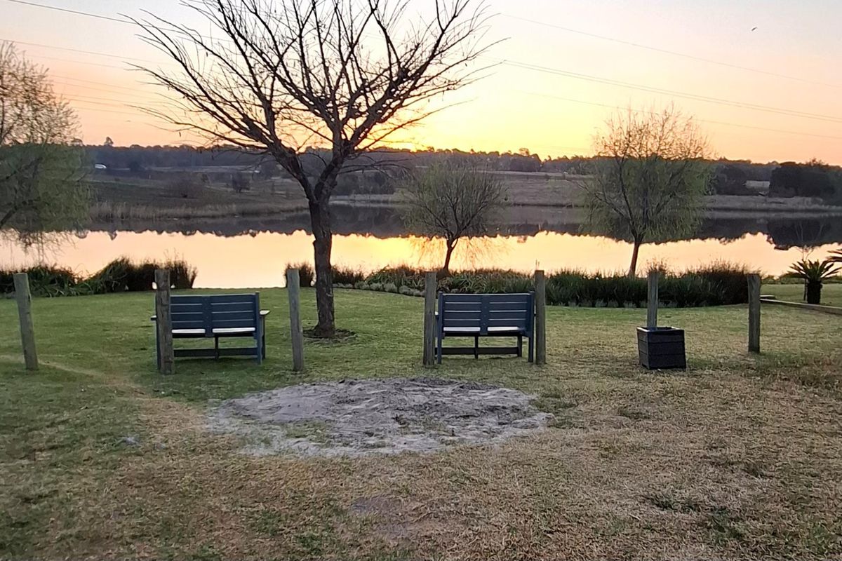 A scenic view of a tranquil lake at sunset, featuring a well-maintained grassy area with mature trees and natural landscaping.