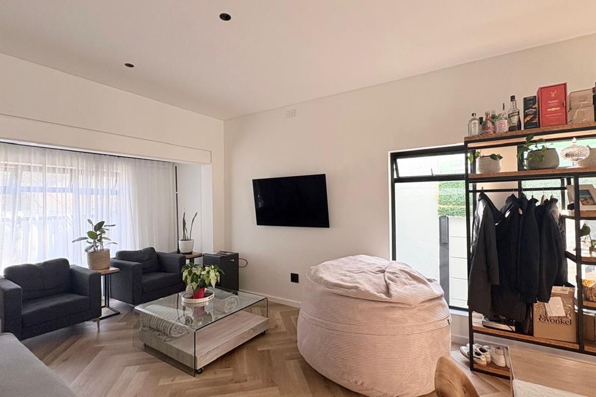 A bright and modern living room featuring herringbone timber flooring, recessed ceiling lighting, and large windows providing ample natural light.