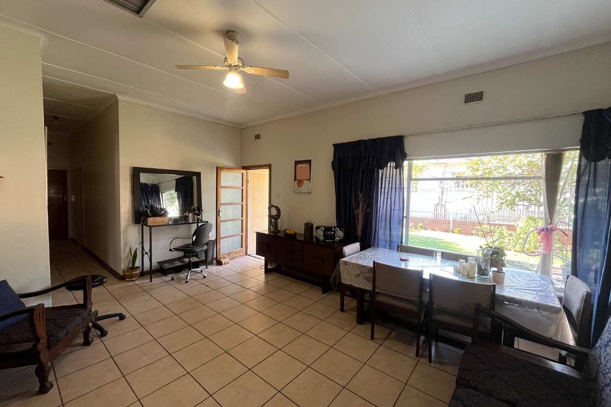 Spacious living and dining area featuring ceramic floor tiles, a ceiling fan, and large windows providing natural light and garden views.