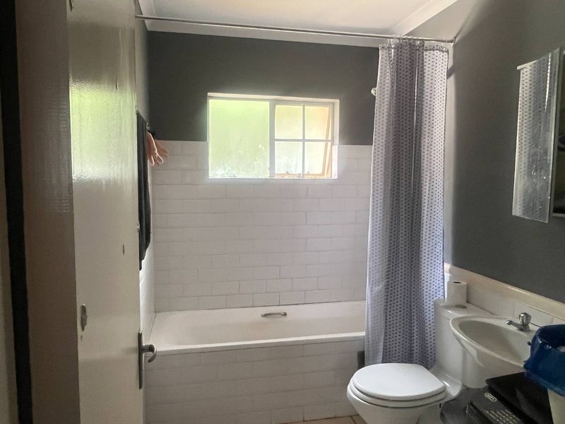 A functional bathroom featuring a bathtub with a shower curtain, a pedestal basin, and a subway tile splashback.