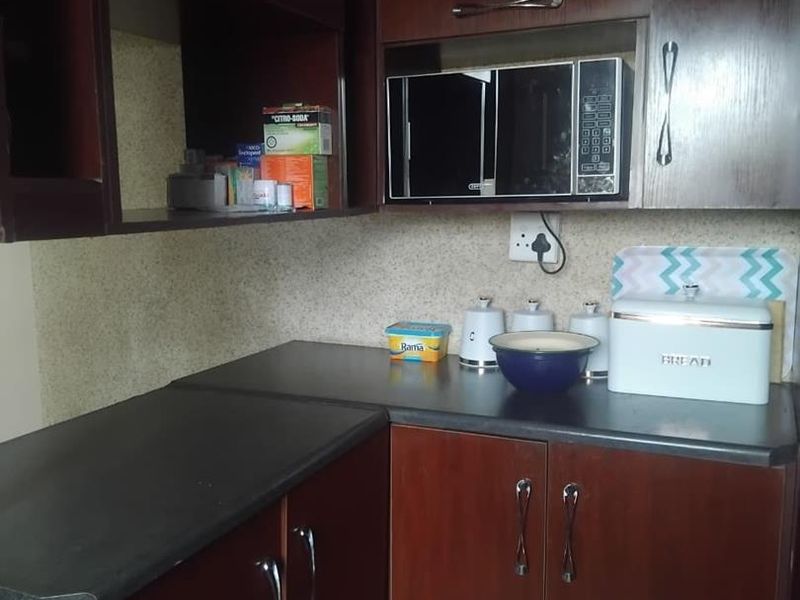 A compact kitchen featuring dark wood cabinetry, laminate countertops, and a built-in microwave, offering functional storage and preparation space.