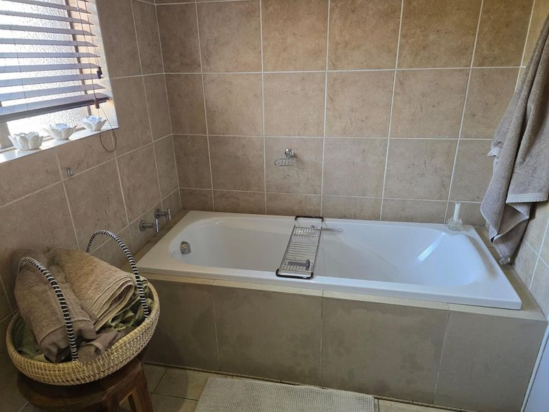 A functional bathroom featuring a built-in bathtub with wall-mounted fixtures and neutral ceramic wall tiling.