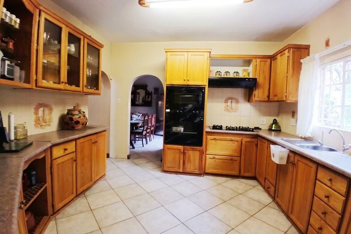 A functional kitchen featuring wooden cabinetry, built-in oven, gas hob, and tiled flooring, offering a classic layout with direct access to the dining area.