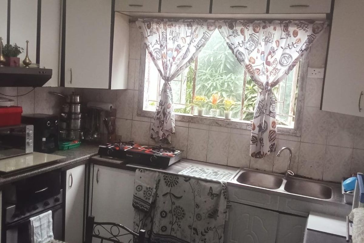 A compact kitchen featuring built-in cabinetry, a double bowl sink, gas hob, and tiled backsplash, offering a functional layout in need of cosmetic updates.