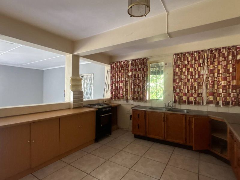 A dated kitchen featuring wooden cabinetry, a double basin sink, and a pass-through window connecting to the adjacent living area.