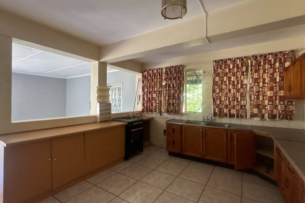 A dated kitchen featuring wooden cabinetry, a double basin sink, and a pass-through window connecting to the adjacent living area.
