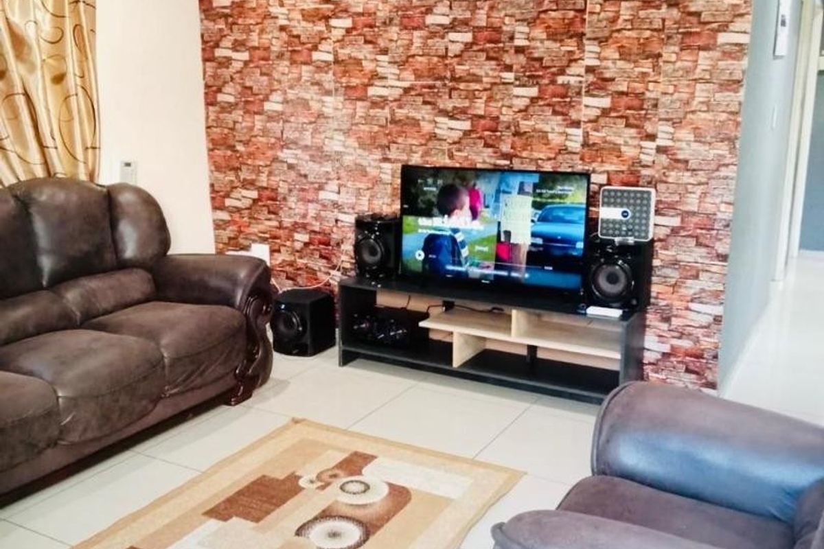 A living room featuring tiled flooring, decorative ceiling cornices, and a brick-effect feature wall.