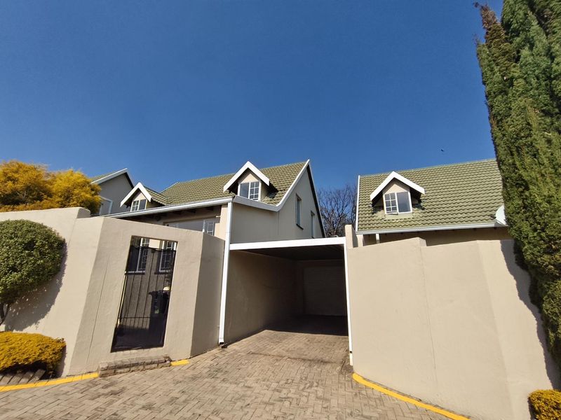 Front elevation of a townhouse featuring a paved driveway, integrated carport, and distinctive dormer windows under a tiled roof.