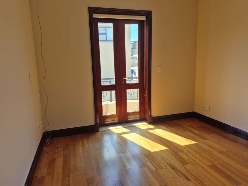 An empty bedroom featuring polished hardwood flooring and classic wooden double doors leading to an outdoor balcony area.