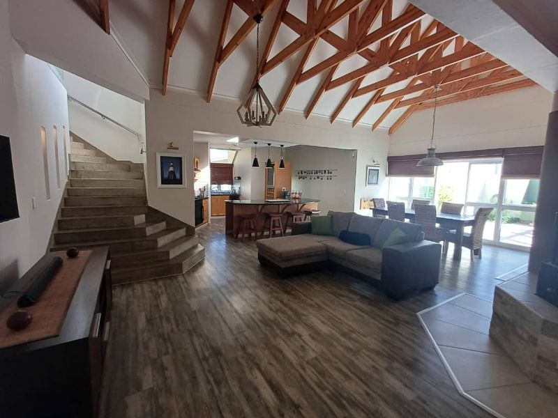 Spacious open-plan living area featuring high vaulted timber ceilings, tiled staircase, wood-look flooring, and a seamless flow to the kitchen and dining space.