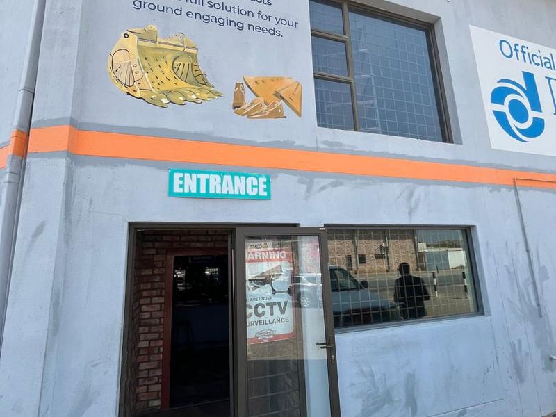 Front entrance of a commercial property featuring aluminium framed glass doors, security window bars, and prominent exterior business signage.