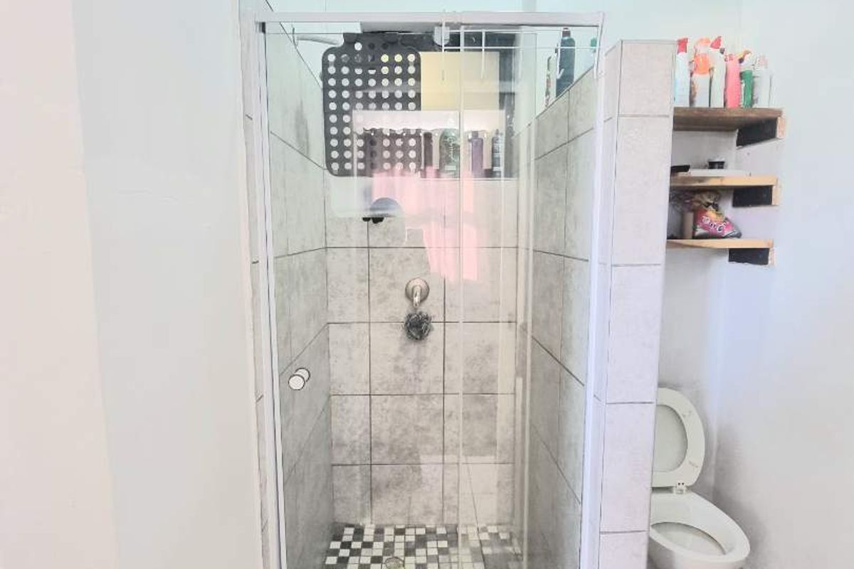 Compact bathroom featuring a glass-enclosed shower with mosaic floor tiling, a standard toilet, and wall-mounted shelving.