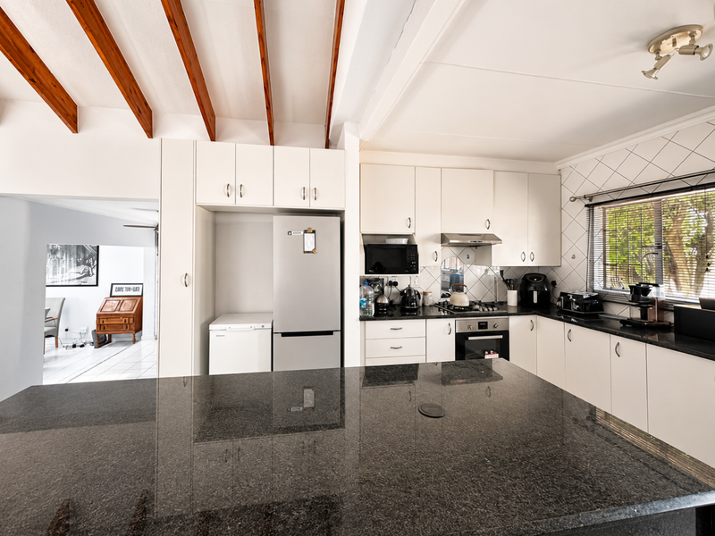 Modern kitchen featuring granite countertops, built-in oven, extractor fan, and distinctive exposed timber ceiling beams, offering a functional and well-lit workspace.