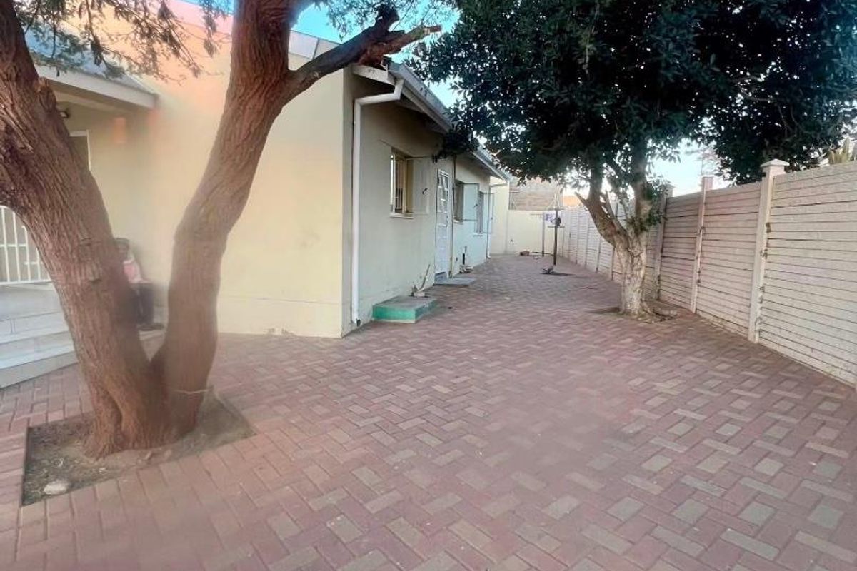 A paved rear courtyard area featuring mature trees and perimeter fencing, providing a functional outdoor space.