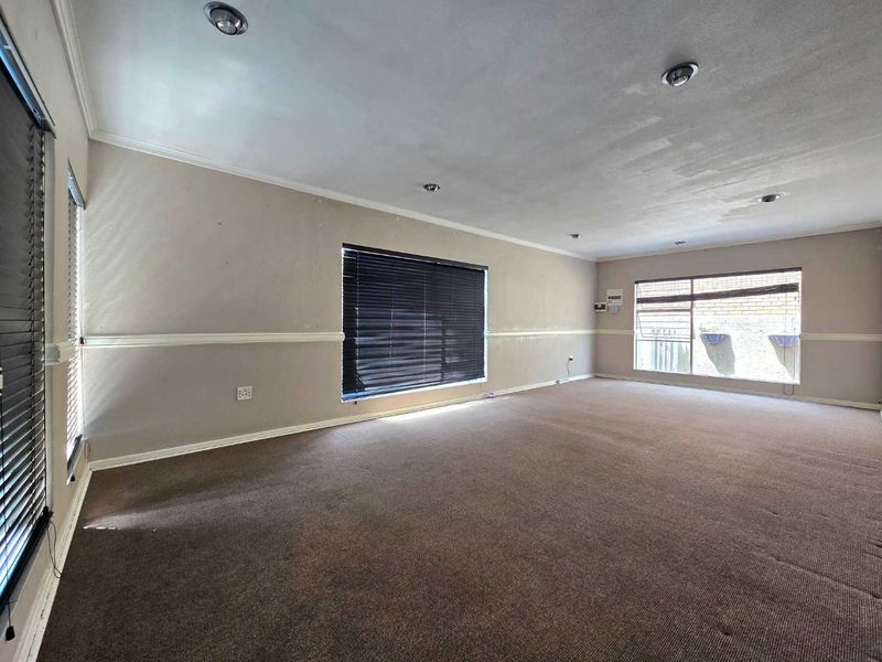 A spacious, empty living room featuring neutral walls with chair rail molding, recessed lighting, and carpeted flooring, ready for personalization.