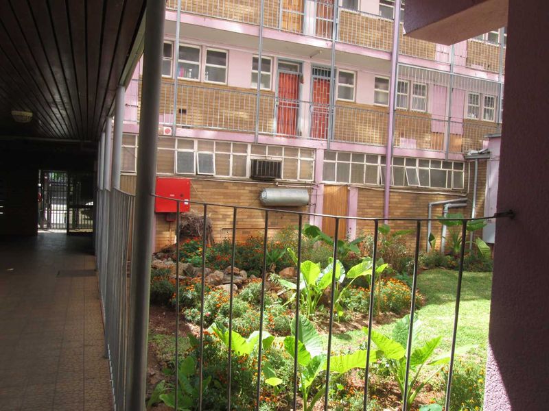 View of the apartment complex rear courtyard featuring a landscaped garden, tiled walkway, and building facade with external utility fixtures.