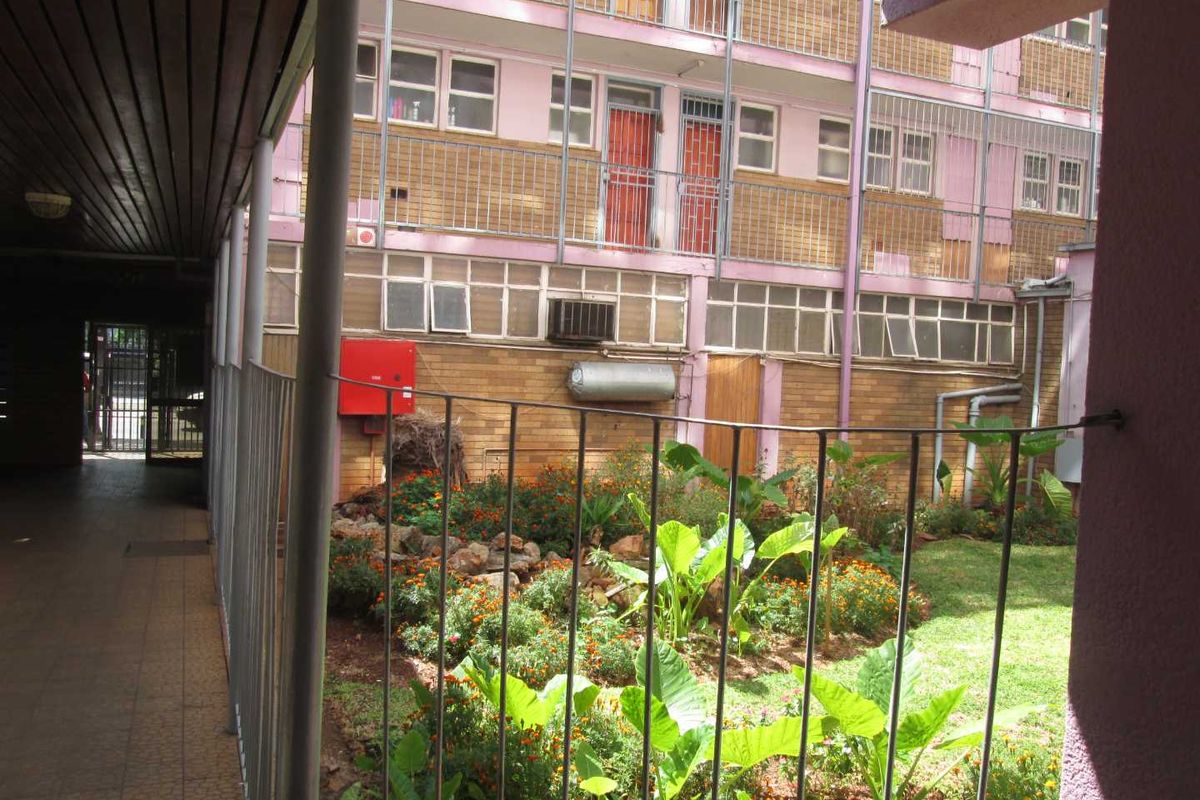 View of the apartment complex rear courtyard featuring a landscaped garden, tiled walkway, and building facade with external utility fixtures.