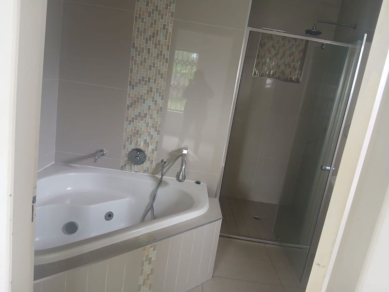 A modern bathroom featuring a corner bathtub with mosaic tile accents and a separate glass-enclosed shower area.