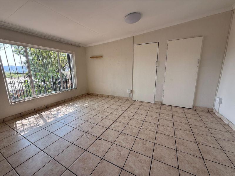 A vacant bedroom featuring tiled flooring, built-in cupboards, and a large window with security bars, offering a clean canvas for personalization.