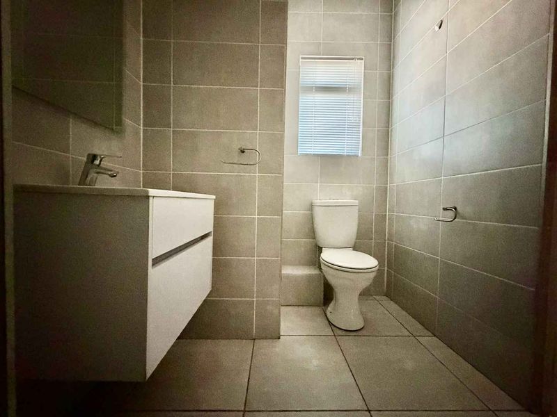 A modern, neutral-toned bathroom featuring a wall-mounted vanity, ceramic basin, and tiled finishes throughout.