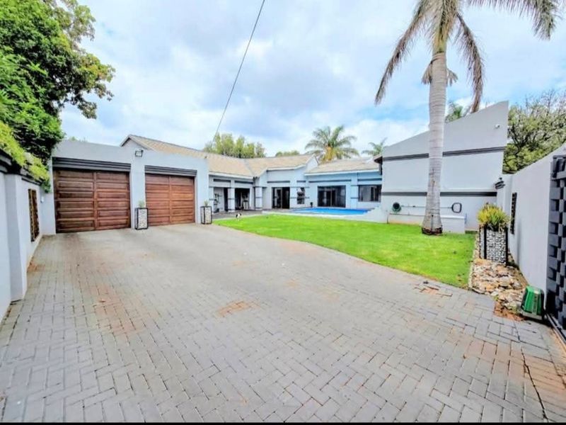 Rear view of the property featuring a paved driveway, double garage, swimming pool, and a well-maintained lawn area.
