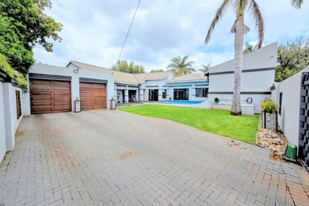 Rear view of the property featuring a paved driveway, double garage, swimming pool, and a well-maintained lawn area.