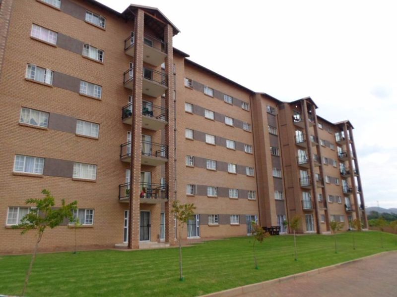 A multi-story apartment building featuring a face brick facade, private balconies with metal railings, and a well-maintained lawn area.
