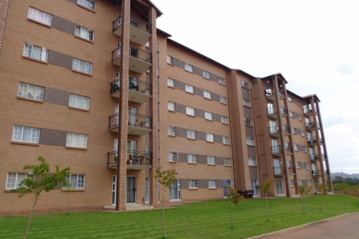 A multi-story apartment building featuring a face brick facade, private balconies with metal railings, and a well-maintained lawn area.
