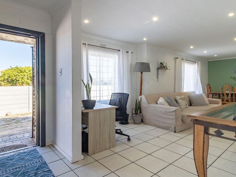An open-plan living and dining area featuring tiled flooring, recessed downlights, and direct access to the exterior through a security gate.