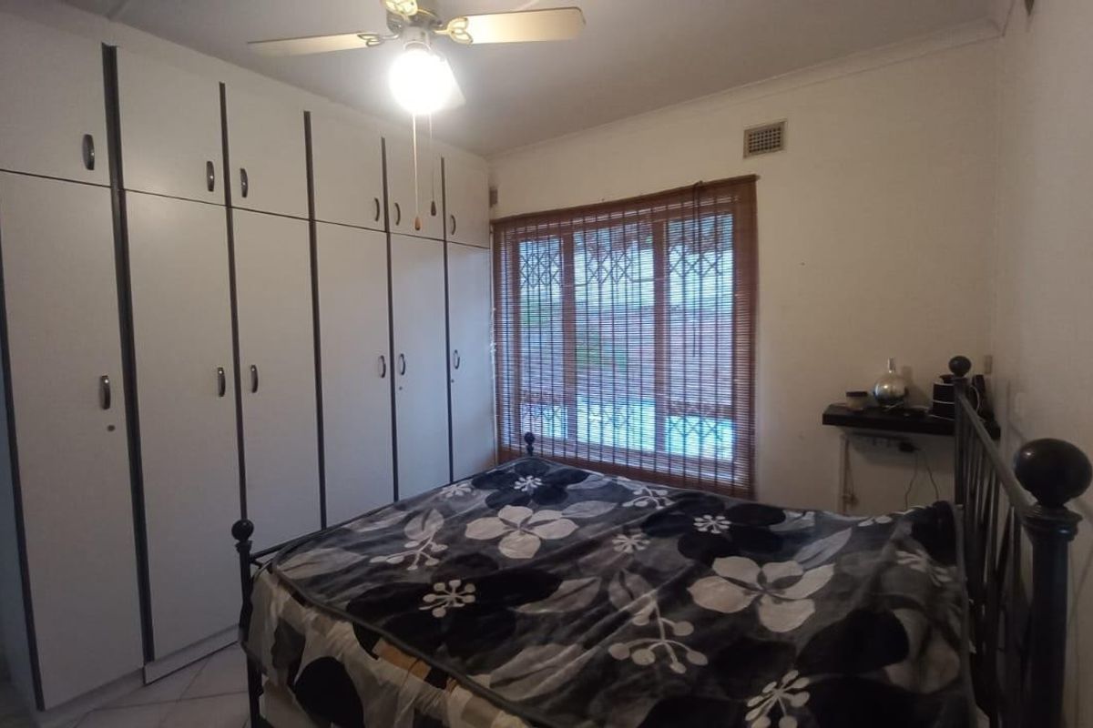 A bedroom featuring extensive built-in cupboards, a ceiling fan, and security bars on the window, providing functional storage and basic security.