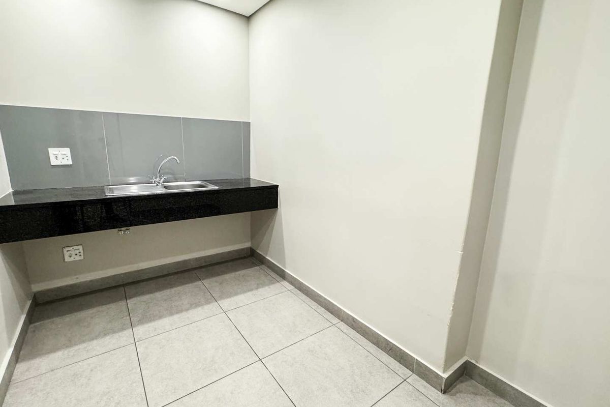 A clean and modern kitchenette area featuring a granite countertop, stainless steel double sink, and neutral tiled flooring.